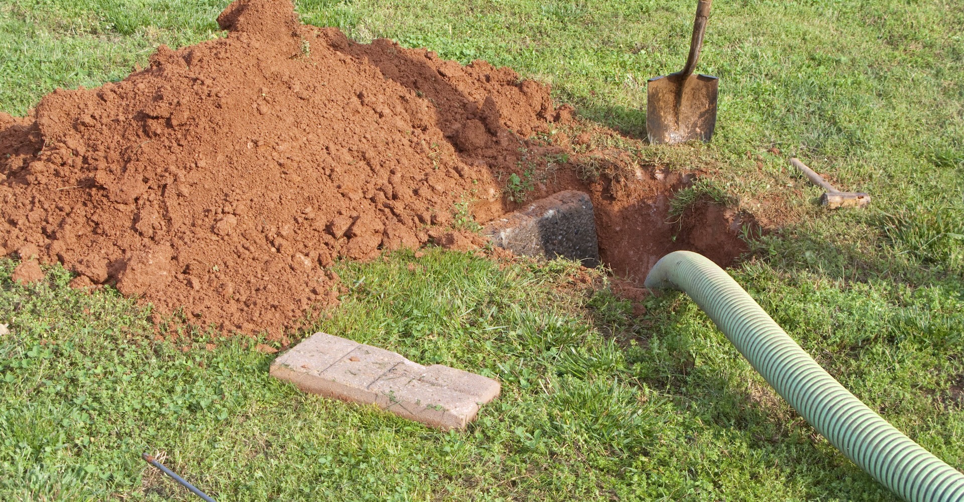 Seen here is a dug out open septic tank being pumped out. All the required tools are laying in the yard.